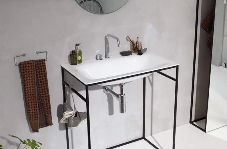 Rechteckiges Waschbecken aus Stahl-Email auf Einbauplatte mit filigranem Metallgestell, Wandarmatur, Seifenspender und Handtuch.