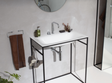 Rechteckiges Waschbecken aus Stahl-Email auf Einbauplatte mit filigranem Metallgestell, Wandarmatur, Seifenspender und Handtuch.