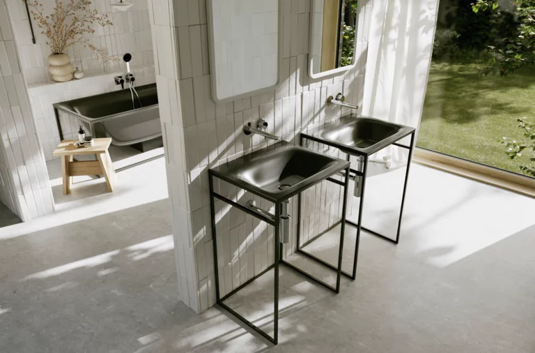 Helles Badezimmer mit zwei dunkelgrauen Waschtischen auf schwarzen Metallgestellen, silberfarbenen Armaturen und Gartenblick.
