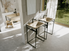 Helles Badezimmer mit zwei beigen Waschtischen auf schwarzen Gestellen, schwarzen Armaturen und Blick in den grünen Garten.