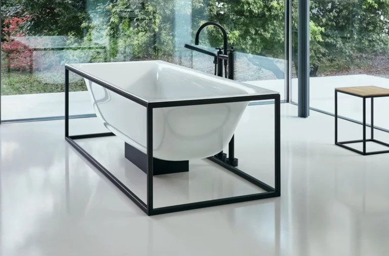 Отдельностоящая прямоугольная ванна из стальной эмали в черном металлическом каркасе, рядом табурет, на фоне большие окна.
