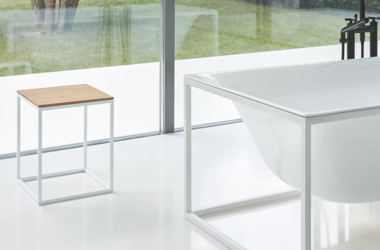 Vrijstaande, rechthoekige badkuip van staal-email met metalen frame, daarnaast krukje met houten zitting, moderne badkamer.