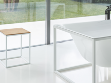 Vrijstaande, rechthoekige badkuip van staal-email met metalen frame, daarnaast krukje met houten zitting, moderne badkamer.