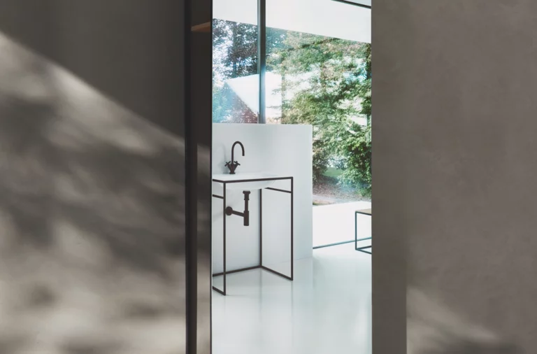 Waschbecken aus Stahl-Email in rechteckiger Form auf Einbauplatte mit schwarzem Gestell vor Fenster mit Ausblick.