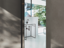 Waschbecken aus Stahl-Email in rechteckiger Form auf Einbauplatte mit schwarzem Gestell vor Fenster mit Ausblick.
