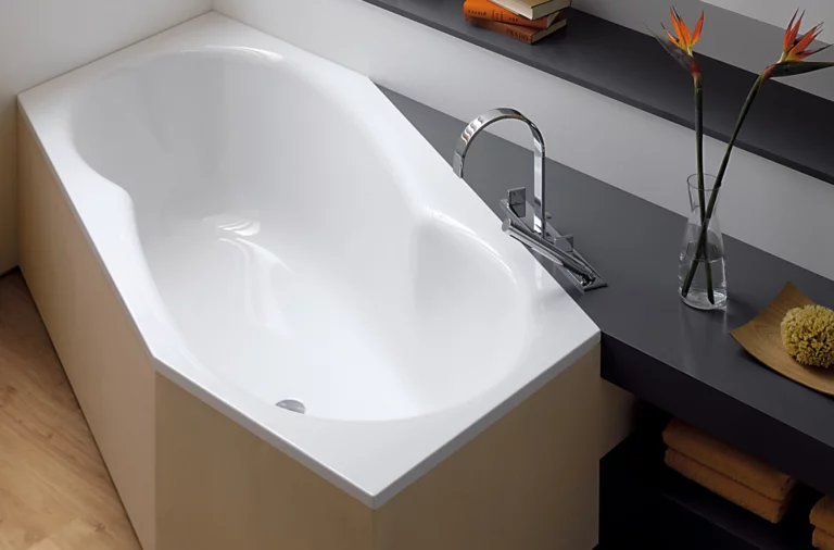 White, asymmetrical steel-enamel bathtub with rounded interior, installed next to dark shelf.