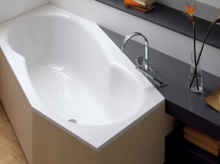 White, asymmetrical steel-enamel bathtub with rounded interior, installed next to dark shelf.