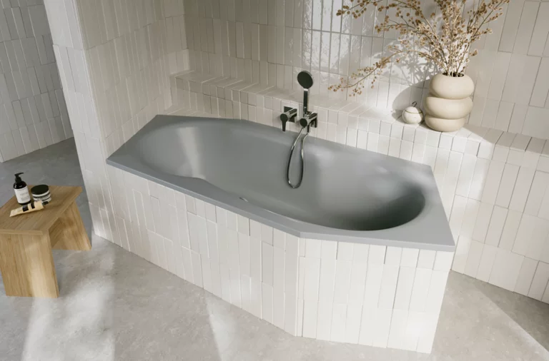 Graue Einbau-Badewanne in hell gefliester Ecke, mit Armatur, Ablage und dekorativer Vase mit Zweigen.