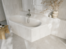 Weiße Einbau-Badewanne in hell gefliester Ecke mit Armatur, Ablagefläche und dekorativer Vase mit Zweigen.