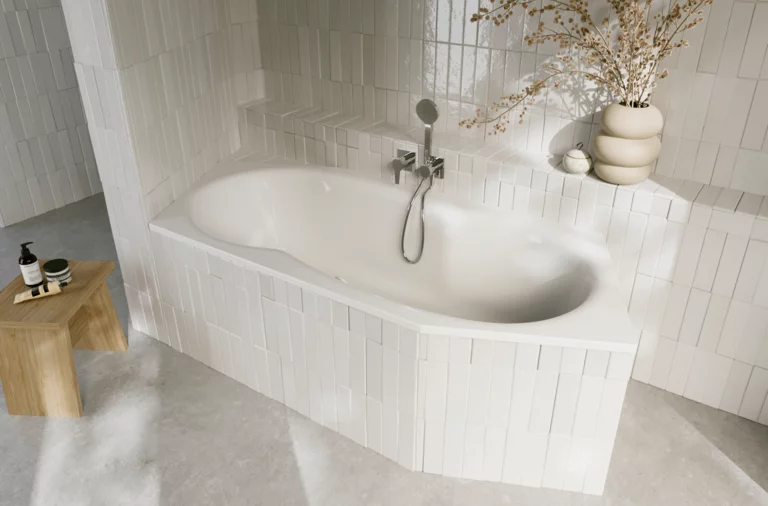 Weiße Einbau-Badewanne in hell gefliester Ecke, mit Armatur, Holzablage und dekorativer Vase mit Zweigen.