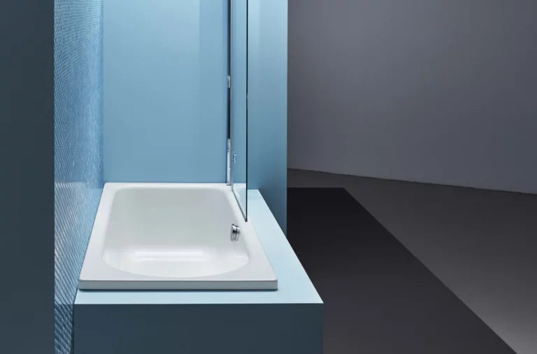 Rechteckige Badewanne aus Stahl-Email, eingebaut in blauer Umgebung, mit seitlicher Duschabtrennung.