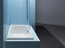 Rechteckige Badewanne aus Stahl-Email, eingebaut in blauer Umgebung, mit seitlicher Duschabtrennung.