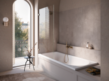 Salle de bains lumineuse avec baignoire-douche, paroi vitrée, robinet doré et vue sur balcon et arbres par haute fenêtre.