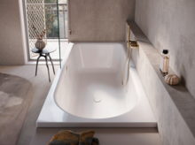 Grande baignoire-douche avec robinet doré, étagère, serviette et vue sur balcon avec table et vase par la fenêtre.