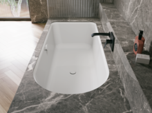 Weiße Badewanne in grauer Badezimmernische mit schwarzer Armatur und eleganter Wandverkleidung.