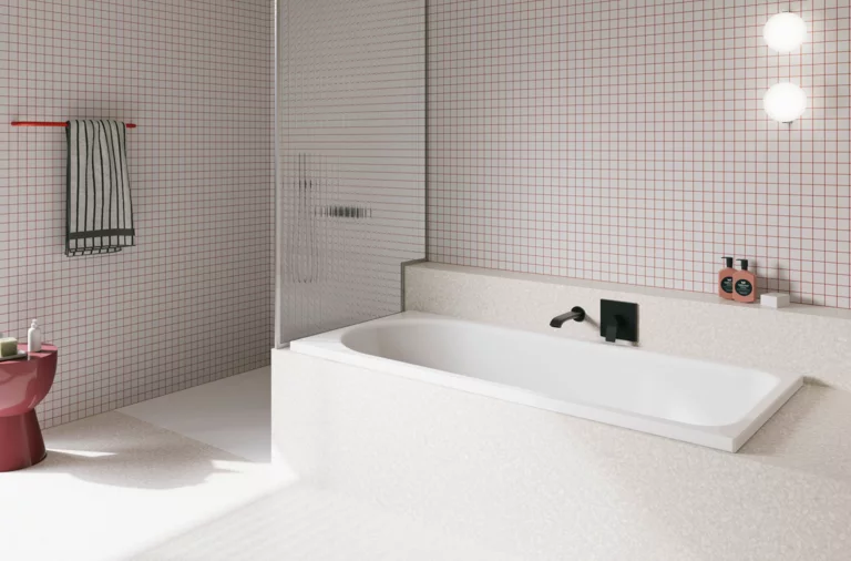 Weiße Badewanne in hell gefliestem Bad mit Wandarmatur, Duschbereich und rosa Hocker.