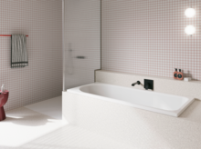 Weiße Badewanne in hell gefliestem Bad mit Wandarmatur, Duschbereich und rosa Hocker.