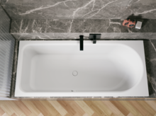Weiße Badewanne in grauer Nische, von oben gesehen, mit schwarzer Armatur und hellem Fischgrätboden.