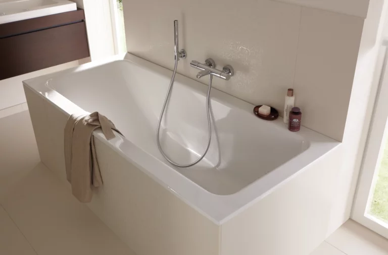 Baignoire rectangulaire blanche en acier émaillé avec douchette, intégrée dans une salle de bain lumineuse.