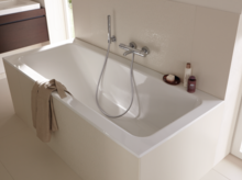 Baignoire rectangulaire blanche en acier émaillé avec douchette, intégrée dans une salle de bain lumineuse.