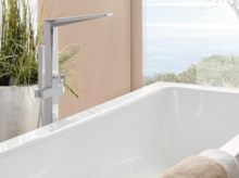 Rechteckige Badewanne aus Stahl-Email mit moderner Armatur, im Vordergrund Handtuch, im Hintergrund Pflanzen und Fenster.