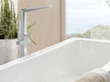 Baignoire rectangulaire en acier émaillé avec robinetterie moderne, serviette au premier plan, plantes et fenêtre à l’arrière-plan.