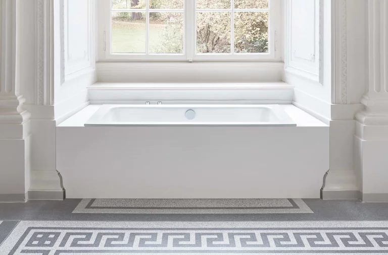 Rechteckige Badewanne aus Stahl-Email, eingebaut in heller Umgebung vor einem großen Fenster, klassische Architektur.