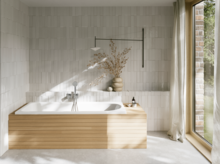 Weiße Badewanne mit gerillter Front in hellem Bad mit weißen Fliesen und großem Fenster.