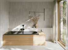 Dunkle Badewanne mit gerillter Front in hellem Bad mit weißen Fliesen und großem Fenster.