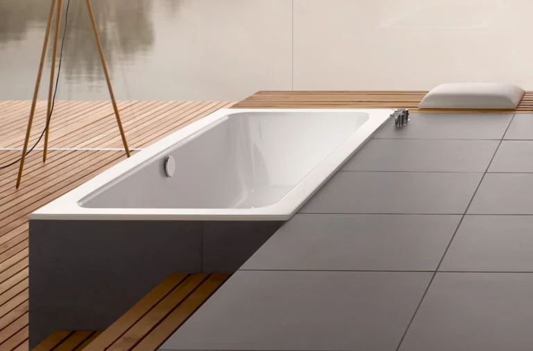 Baignoire rectangulaire en acier émaillé, partiellement encastrée dans un sol en bois, avec entourage moderne en carrelage.