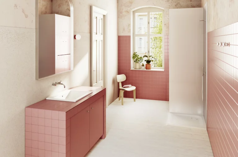 Светлая ванная с розовой плиткой, душ справа, окно с растениями и стулом на заднем плане.