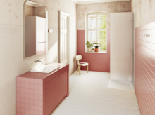 Светлая ванная с розовой плиткой, душ справа, окно с растениями и стулом на заднем плане.