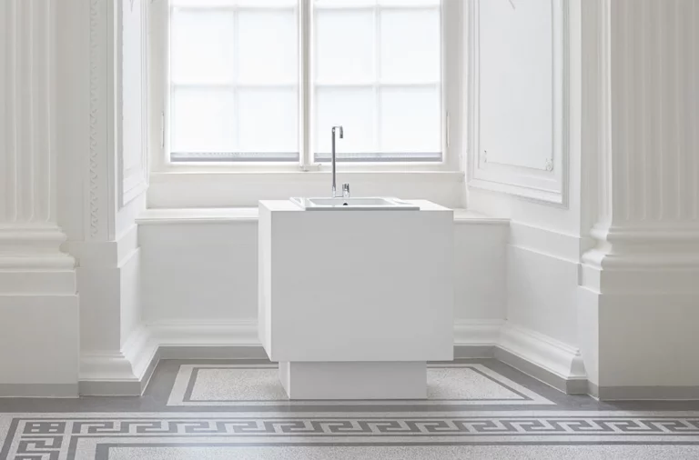 Waschbecken aus Stahl-Email auf rechteckiger Einbauplatte mit hoher Armatur, vor großem Fenster, minimalistisches Design.