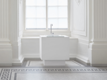 Раковина из стальной эмали на прямоугольной столешнице с высоким смесителем у большого окна, минималистичный дизайн.