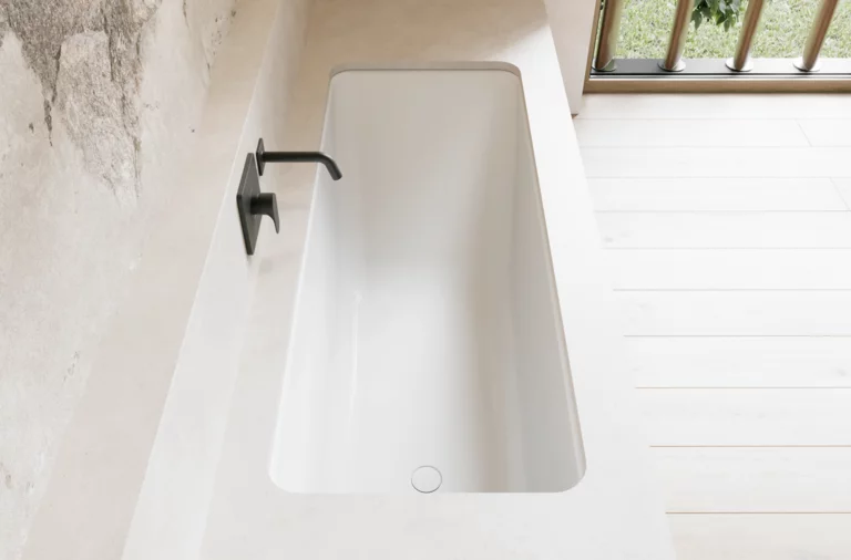 Weiße Badewanne in heller Nische mit schwarzer Wandarmatur und großem Fenster daneben.
