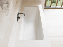 Weiße Badewanne in heller Nische mit schwarzer Wandarmatur und großem Fenster daneben.
