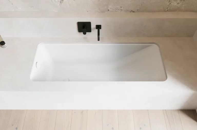 Weiße Badewanne in heller Nische mit schwarzer Wandarmatur und hellem Boden.