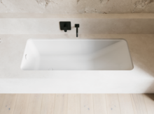 Weiße Badewanne in heller Nische mit schwarzer Wandarmatur und hellem Boden.