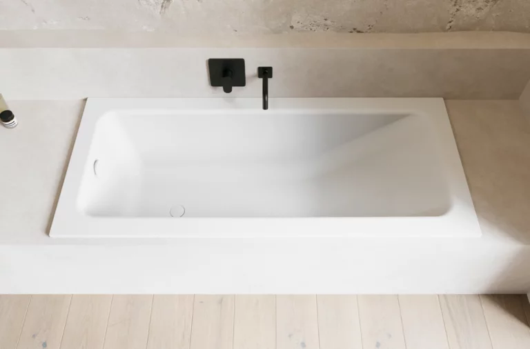 Weiße Badewanne in heller Nische mit schwarzer Wandarmatur und hellem Holzboden.