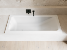 Weiße Badewanne in heller Nische mit schwarzer Wandarmatur und hellem Holzboden.