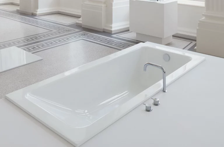 Rechteckige Badewanne aus Stahl-Email mit abgerundeten Ecken, eingebaut in weiße Fläche, moderner Wasserhahn.
