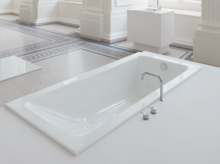 Rechteckige Badewanne aus Stahl-Email mit abgerundeten Ecken, eingebaut in weiße Fläche, moderner Wasserhahn.