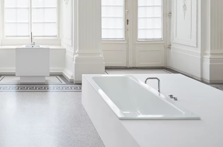 Rechteckige Stahl-Email-Badewanne, eingelassen in eine weiße Fläche, im hellen, klassischen Badezimmer mit Einbauplatte und Waschbecken.
