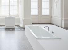 Rechteckige Stahl-Email-Badewanne, eingelassen in eine weiße Fläche, im hellen, klassischen Badezimmer mit Einbauplatte und Waschbecken.