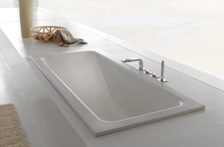 Прямоугольная стальная эмалированная ванна, встроена в белую поверхность, с современной арматурой и минималистичным дизайном.