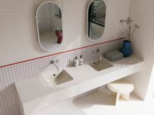 Helles Badezimmer mit zwei beigen Waschtischen, silberfarbenen Wandarmaturen, zwei ovalen Spiegeln und blauer Vase.