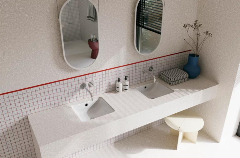 Helles Badezimmer mit zwei weißen Waschtischen, silberfarbenen Wandarmaturen, zwei ovalen Spiegeln und blauer Vase.