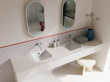 Helles Badezimmer mit zwei weißen Waschtischen, silberfarbenen Wandarmaturen, zwei ovalen Spiegeln und blauer Vase.