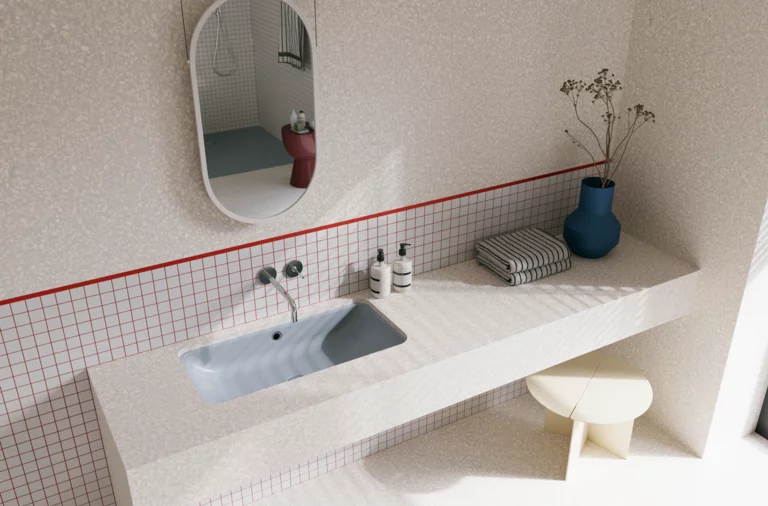 Helles Badezimmer mit blaugrauem Waschtisch, silberfarbenen Wandarmaturen, ovalem Spiegel und blauer Vase.