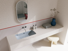 Helles Badezimmer mit blaugrauem Waschtisch, silberfarbenen Wandarmaturen, ovalem Spiegel und blauer Vase.